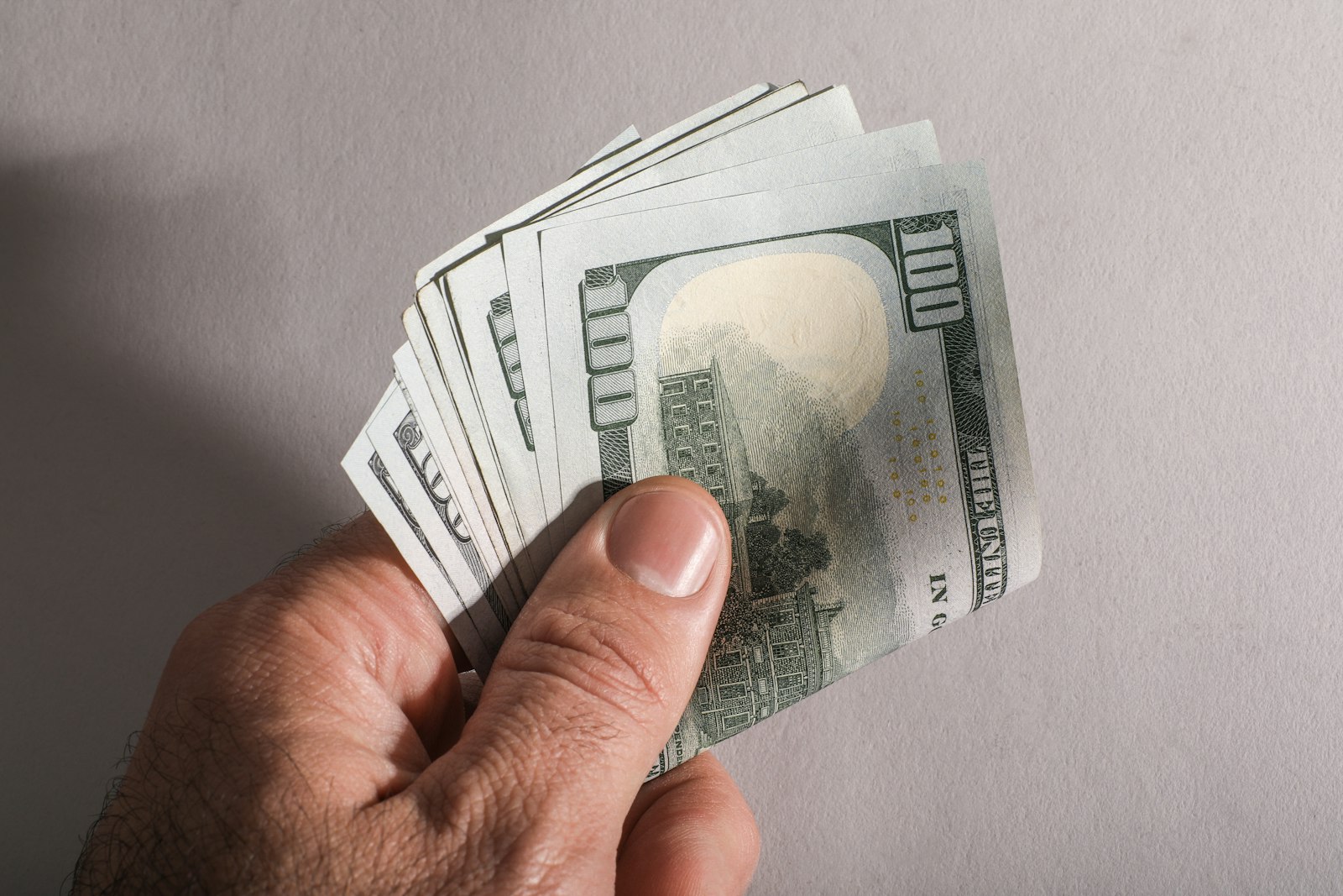 A hand holding a fan of one hundred dollar bills
