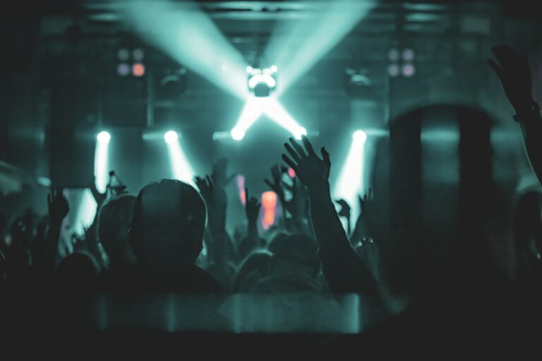 A silhouetted crowd with hands raised under concert stage lights