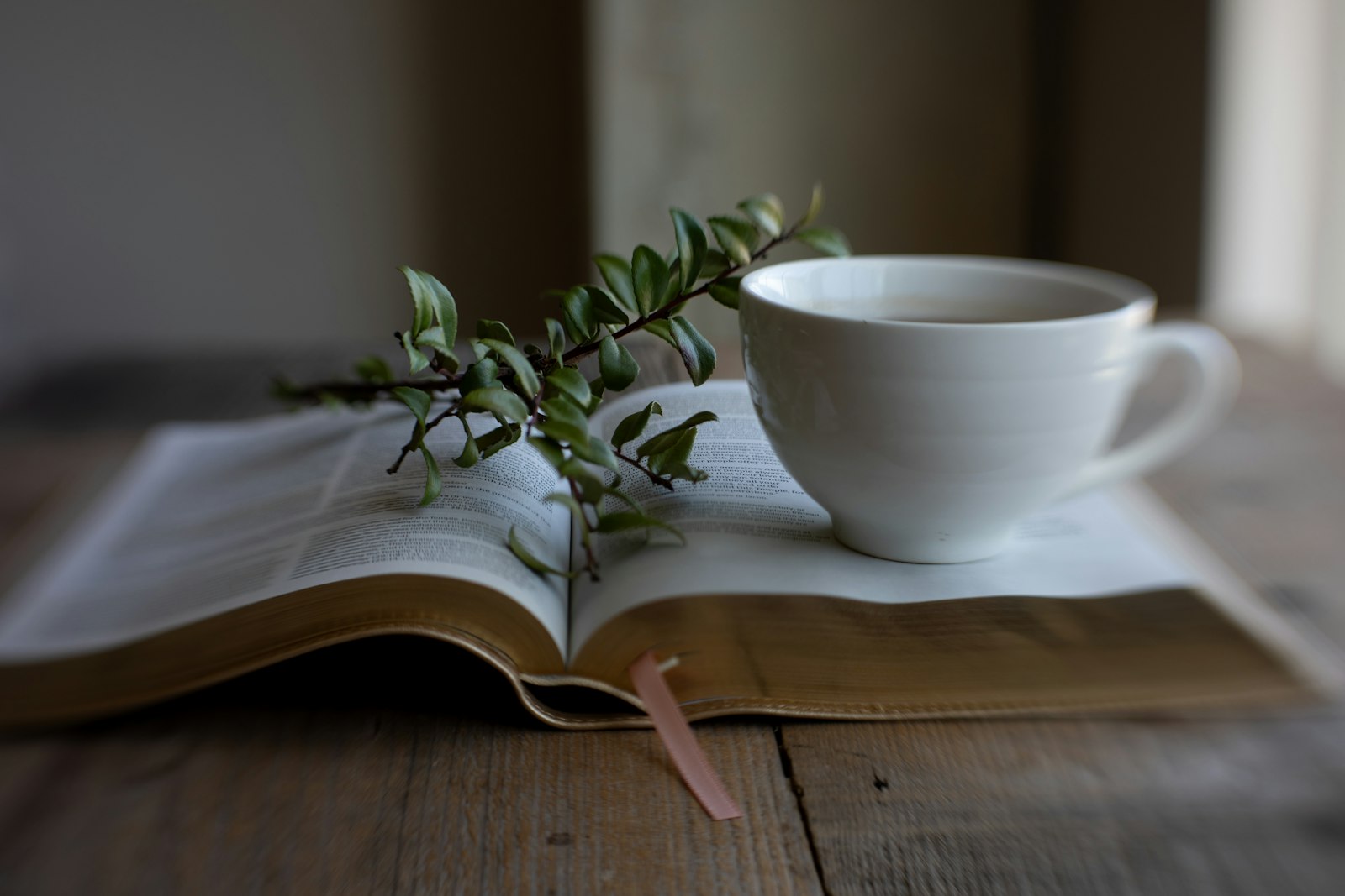 An open Bible on a wooden table beside a cup of coffee