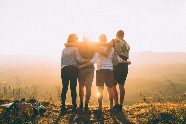 Four friends with arms around each other watching the sunset