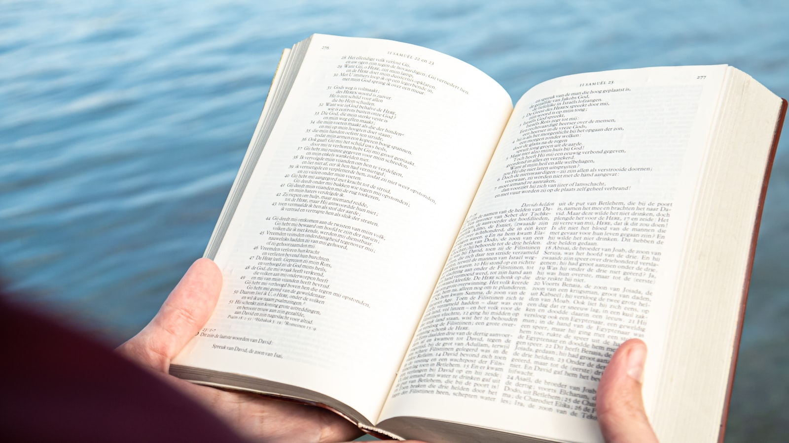 Hands holding an open Bible beside the water