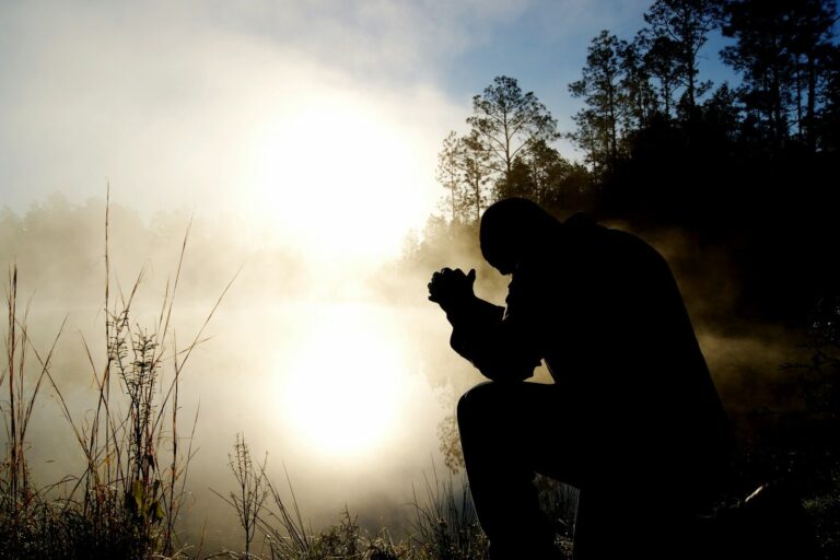 A man kneeling in prayer by a misty lake at sunrise