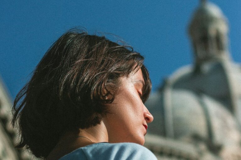 A woman in profile, eyes closed, with a cathedral rising behind her